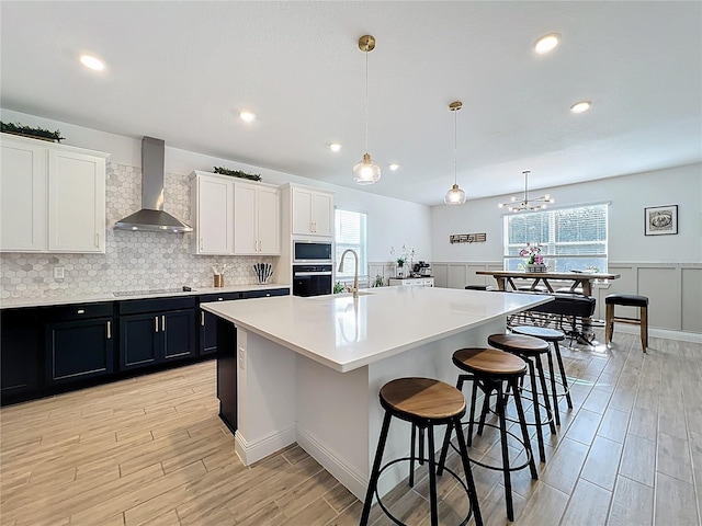 2044 Keystone Pass Blvd, Minneola, FL 34715 - kitchen with wall chimney exhaust hood, black appliances, light countertops, a breakfast bar area, and light wood-style floors