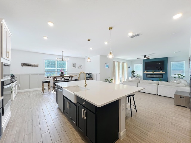 2044 Keystone Pass Blvd, Minneola, FL 34715 - kitchen featuring dark cabinets, light countertops, light wood-type flooring, a ceiling fan, and an island with sink