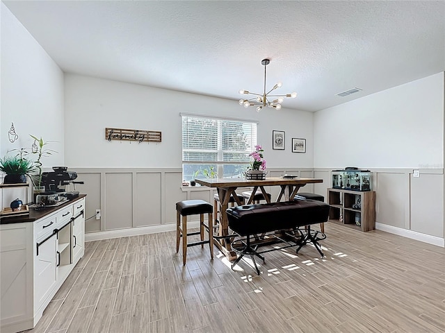 2044 Keystone Pass Blvd, Minneola, FL 34715 - dining area with a decorative wall, light wood finished floors, a chandelier, a wainscoted wall, and a textured ceiling