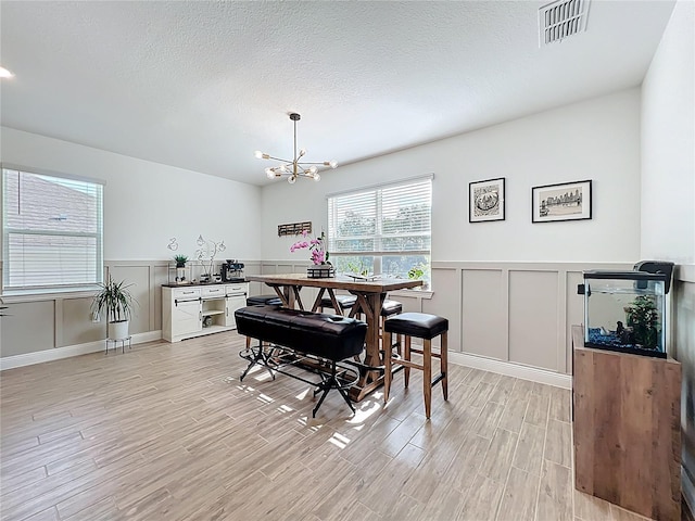 2044 Keystone Pass Blvd, Minneola, FL 34715 - dining room featuring a chandelier, light wood-style flooring, a decorative wall, a wainscoted wall, and a textured ceiling