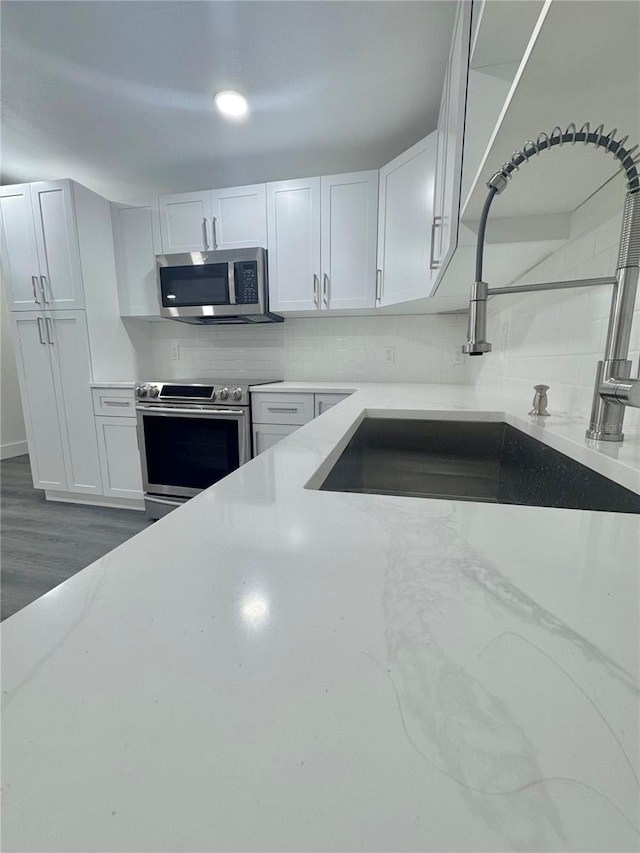 4934 Avery Rd, New Port Richey, FL 34652 - kitchen with stainless steel appliances, tasteful backsplash, white cabinets, light stone counters, and dark wood-style flooring