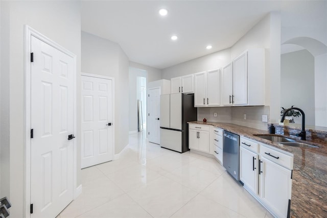 9844 Montclair Cir, Apopka, FL 32703 - kitchen with stainless steel dishwasher, freestanding refrigerator, dark stone countertops, white cabinetry, and arched walkways