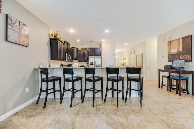 kitchen featuring a kitchen bar, stainless steel appliances, kitchen peninsula, dark brown cabinetry, and light tile patterned flooring