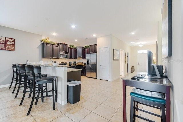 kitchen with a kitchen bar, kitchen peninsula, light tile patterned flooring, dark brown cabinets, and appliances with stainless steel finishes