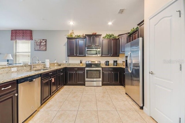 kitchen featuring stainless steel appliances, light stone counters, dark brown cabinetry, sink, and light tile patterned flooring