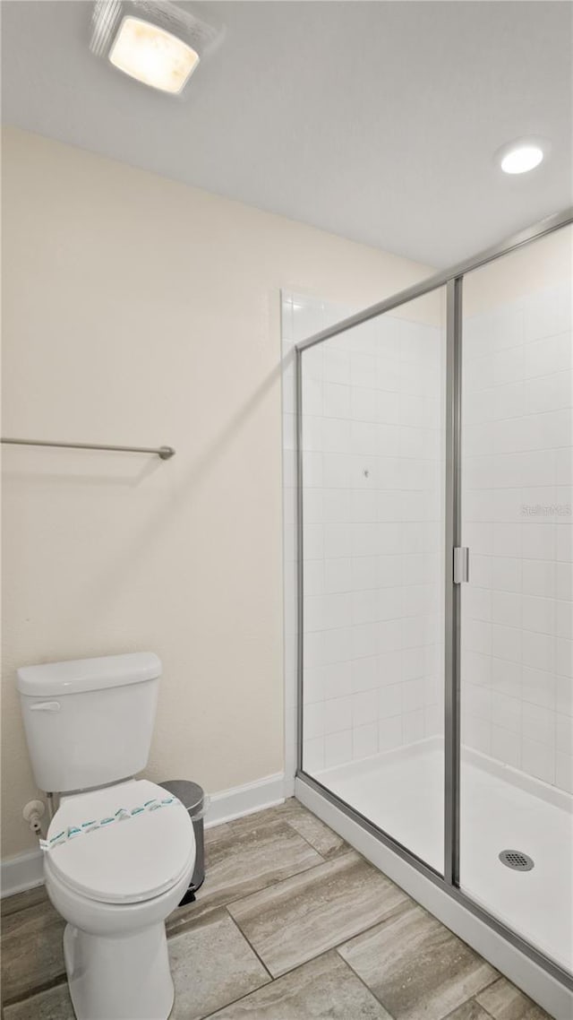 bathroom with hardwood / wood-style floors, toilet, and a shower with door