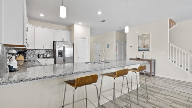 kitchen with decorative backsplash, stainless steel fridge with ice dispenser, white cabinets, and hanging light fixtures