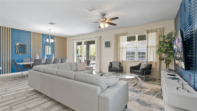 living room featuring a textured ceiling and ceiling fan with notable chandelier