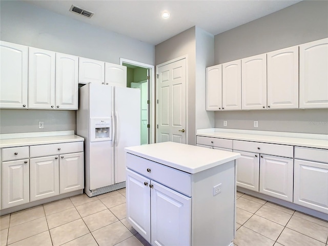 kitchen with light tile patterned floors, white refrigerator with ice dispenser, a center island, and white cabinets