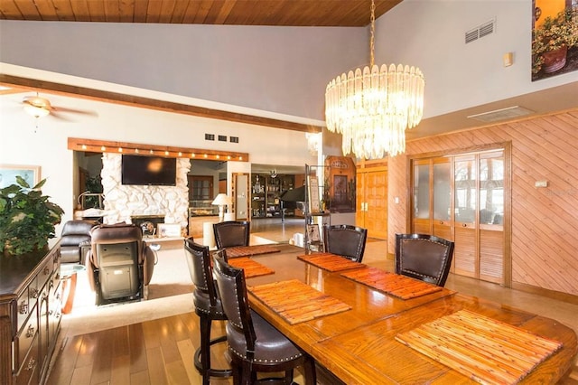 dining area featuring a stone fireplace, wooden ceiling, wood-type flooring, and ceiling fan with notable chandelier