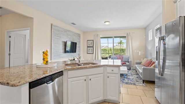 kitchen with sink, light stone counters, white cabinets, appliances with stainless steel finishes, and light tile flooring