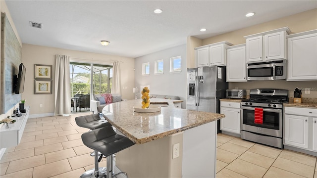 kitchen with stainless steel appliances, a center island, light stone countertops, and white cabinets