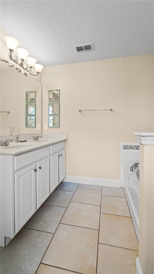 bathroom with tile patterned floors, a textured ceiling, vanity, a bathtub, and a notable chandelier