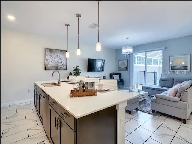 kitchen with sink, an inviting chandelier, decorative light fixtures, a kitchen island with sink, and dark brown cabinets