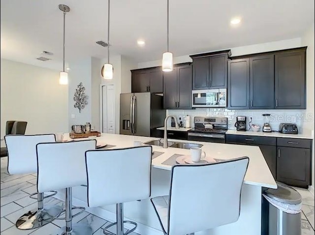 kitchen featuring hanging light fixtures, stainless steel appliances, a kitchen island with sink, and sink