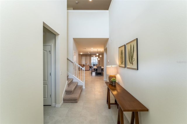 hallway with an inviting chandelier, light tile floors, and a high ceiling