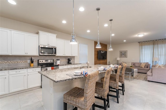 kitchen featuring an island with sink, a kitchen bar, appliances with stainless steel finishes, white cabinets, and hanging light fixtures