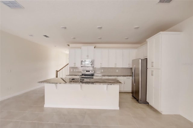 kitchen with stone countertops, stainless steel appliances, a center island with sink, and white cabinets