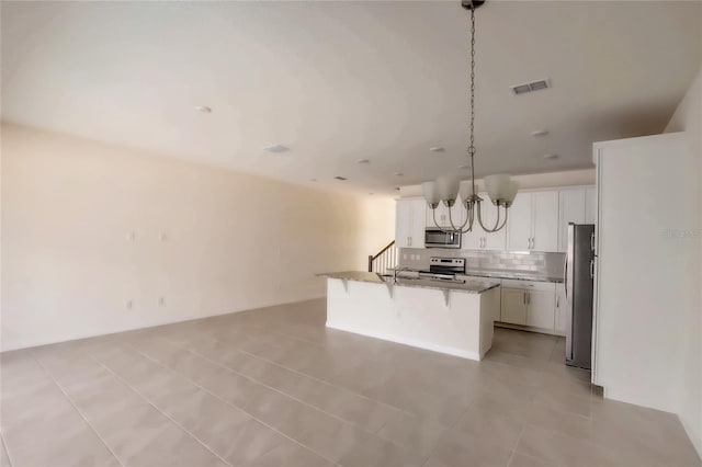 kitchen featuring appliances with stainless steel finishes, a kitchen bar, pendant lighting, white cabinets, and a kitchen island with sink