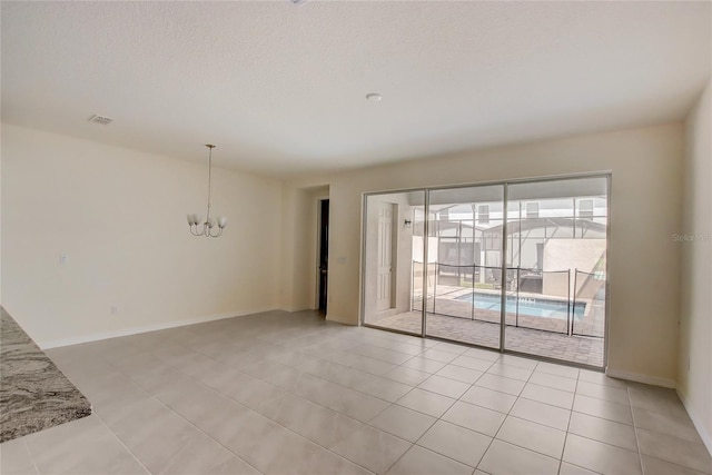 empty room with a chandelier, a textured ceiling, and light tile patterned floors