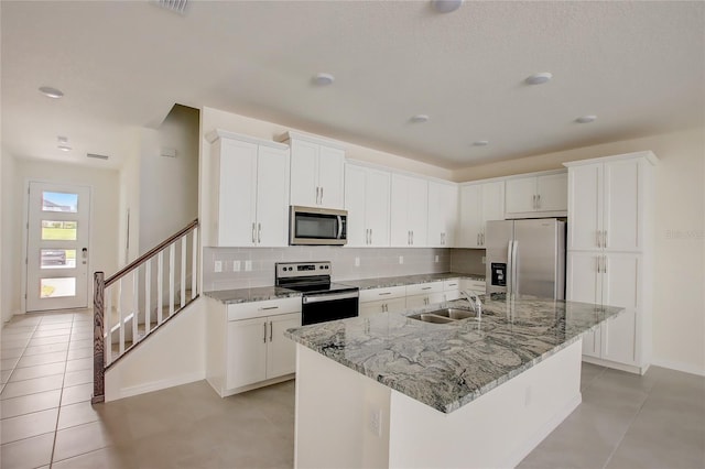 kitchen with tasteful backsplash, appliances with stainless steel finishes, sink, an island with sink, and white cabinets