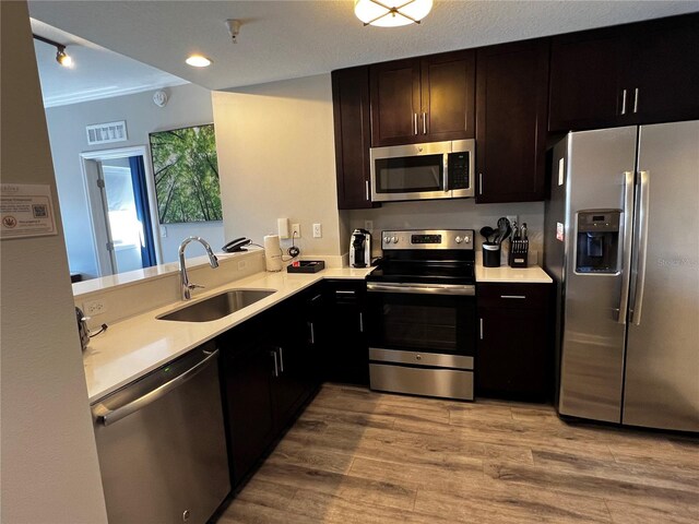 kitchen with sink, light hardwood / wood-style flooring, stainless steel appliances, ornamental molding, and kitchen peninsula