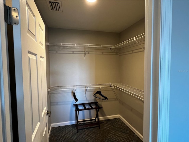 walk in closet featuring dark carpet