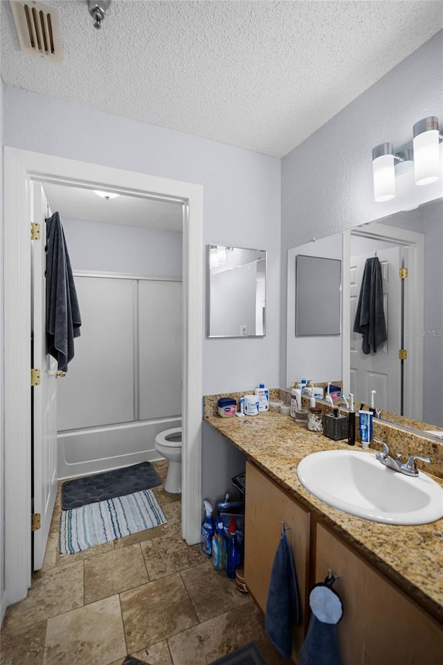 full bathroom featuring toilet, a textured ceiling, vanity, enclosed tub / shower combo, and tile floors