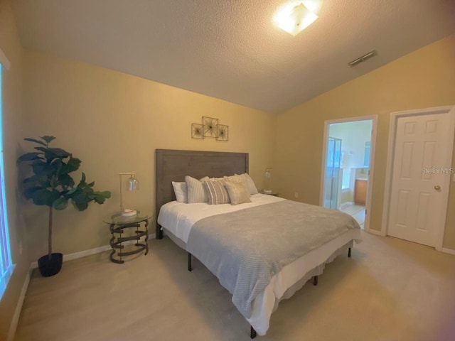 bedroom featuring a textured ceiling, lofted ceiling, ensuite bath, and light colored carpet