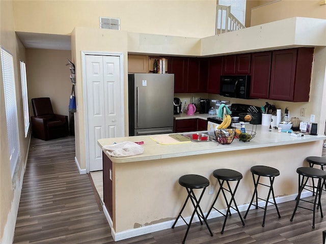 kitchen featuring a kitchen bar, dark wood-type flooring, stainless steel refrigerator, and range