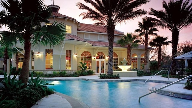 pool at dusk featuring a patio area and french doors