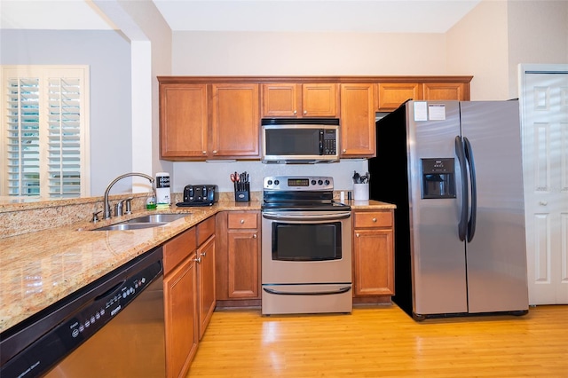 kitchen with light stone countertops, light hardwood / wood-style flooring, appliances with stainless steel finishes, and sink