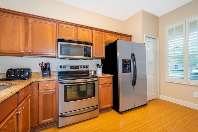 kitchen with stainless steel appliances, light wood-type flooring, and light stone counters