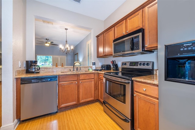 kitchen with ceiling fan with notable chandelier, light hardwood / wood-style flooring, appliances with stainless steel finishes, sink, and light stone counters