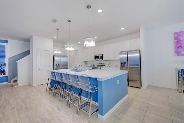 kitchen featuring stainless steel appliances, decorative light fixtures, white cabinetry, a kitchen bar, and a kitchen island with sink