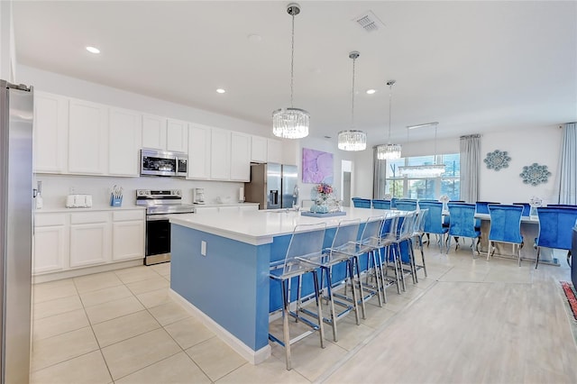 kitchen featuring a kitchen breakfast bar, stainless steel appliances, an island with sink, pendant lighting, and white cabinetry