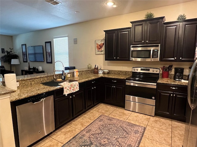 kitchen featuring sink, stainless steel appliances, light stone counters, light tile patterned flooring, and kitchen peninsula