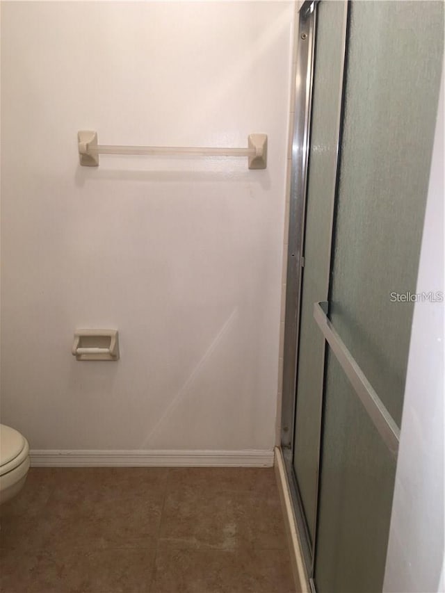 bathroom featuring toilet, tile patterned flooring, and a shower with door