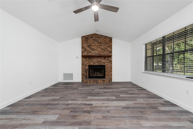 unfurnished living room featuring brick wall, dark hardwood / wood-style floors, ceiling fan, a fireplace, and vaulted ceiling