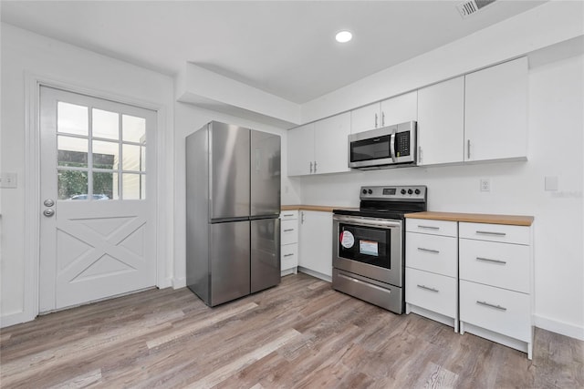 kitchen with white cabinets, wood counters, stainless steel appliances, and light hardwood / wood-style flooring