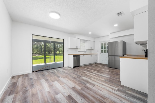 kitchen with white cabinets, a textured ceiling, appliances with stainless steel finishes, and light hardwood / wood-style flooring