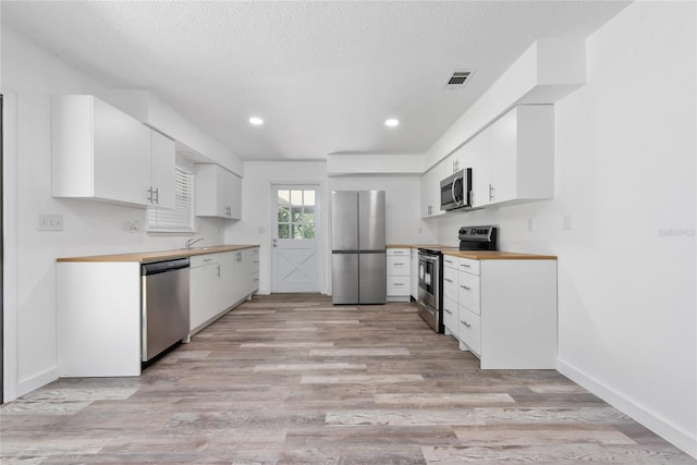 kitchen with white cabinets, appliances with stainless steel finishes, light hardwood / wood-style floors, and butcher block counters