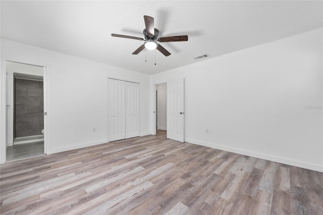 unfurnished bedroom featuring a closet, light hardwood / wood-style floors, ceiling fan, and ensuite bathroom