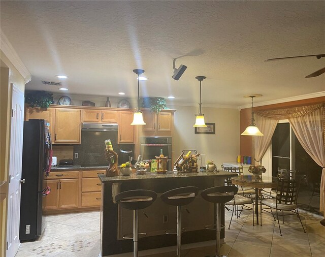 kitchen with light tile floors, a kitchen bar, black refrigerator, ceiling fan, and crown molding