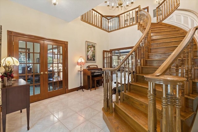 staircase featuring a chandelier, a towering ceiling, light tile flooring, and french doors