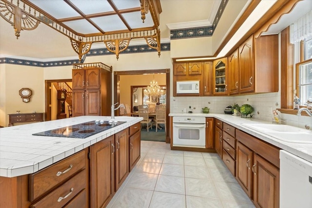 kitchen featuring backsplash, white appliances, a notable chandelier, sink, and an island with sink