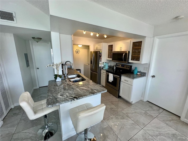 kitchen with sink, dark stone countertops, white cabinets, appliances with stainless steel finishes, and a kitchen bar