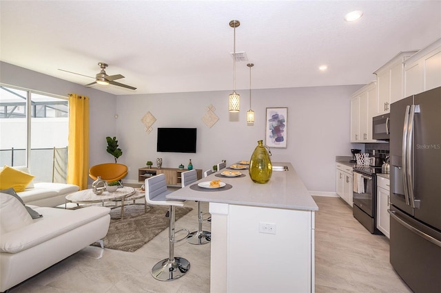 kitchen with a center island, ceiling fan, a breakfast bar, appliances with stainless steel finishes, and white cabinets