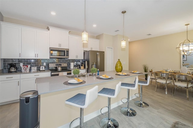 kitchen with decorative light fixtures, a kitchen breakfast bar, light wood-type flooring, stainless steel appliances, and tasteful backsplash