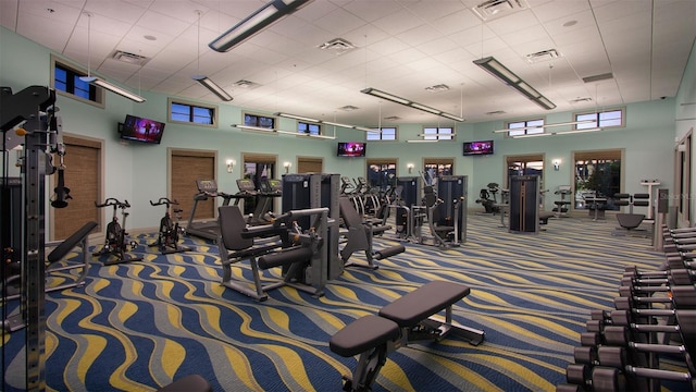 gym featuring a paneled ceiling, dark carpet, and a towering ceiling